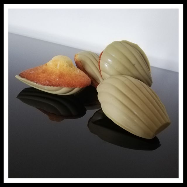 Per fare questo effetto sciogliere 100 g di ciocolato bianco e aggiungere 1 cucchiaino di pasta di pistacchio.Inserire il composto in uno stampo di silicone con conchiglie e appoggiare sopra la madeleine. Porre in frigorifero per 8 minuti. Sformare le Madeleines